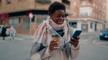 Genç Afrikalı Amerikalı kadın akıllı telefon kullanıyor. Sokakta kahve içiyor.