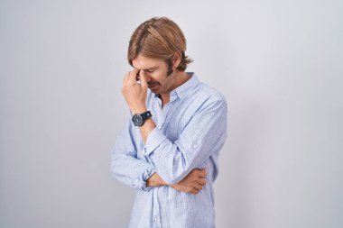 Beyaz arka planda duran beyaz bıyıklı, burnu ve gözleri ovuşturmaktan yorgun düşmüş, yorgun ve baş ağrısı çeken beyaz bir adam. Stres ve hüsran kavramı. 