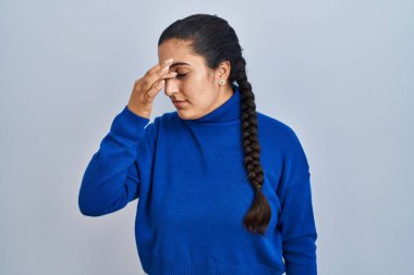 Young hispanic woman standing over isolated background tired rubbing nose and eyes feeling fatigue and headache. stress and frustration concept. 