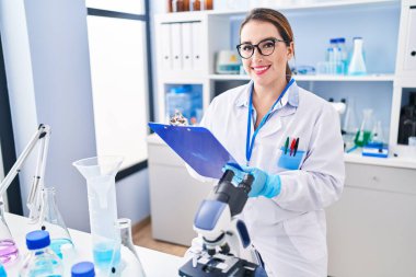 Young beautiful hispanic woman scientist writing report working at laboratory
