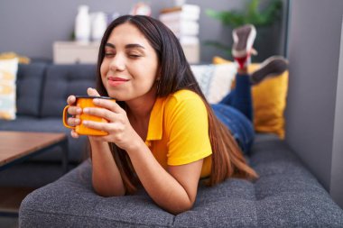 Young beautiful arab woman drinking coffee lying on sofa at home