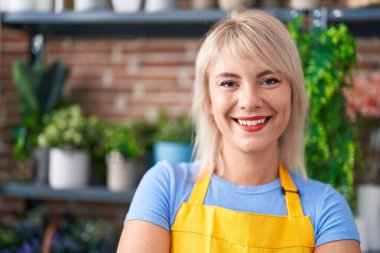 Çiçekçiye bakıp gülümseyen genç sarışın kadın.