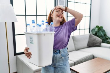 Genç kızıl saçlı kadın elinde plastik şişelerle geri dönüşüm sepetini tutuyor. Kendine güvenen, el hareketleriyle saçlarına dokunan, çekici ve modaya uygun poz veren. 