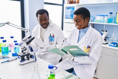 Erkek ve kadın bilim adamları laboratuvarda mikroskop kullanarak not defteri kullanıyorlar.