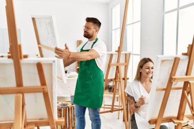 Sanat stüdyosunda gülümseyen beyaz bir çift. Adam ayakta ve tuvali tutuyor..