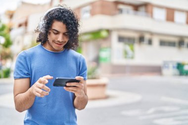 Sokakta video oyunu oynarken kendinden emin gülümseyen genç Latin adam.