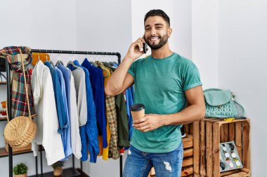 Genç Arap müşteri akıllı telefondan konuşuyor giyim mağazasında elbise rafının yanında duruyor.