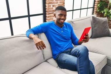 Young african american man using touchpad sitting on sofa at home