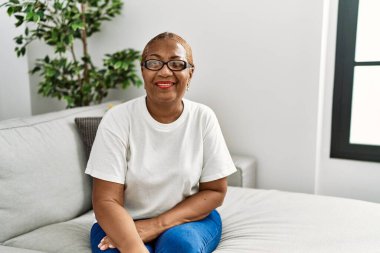 Olgun İspanyol kadın evinde koltukta oturmuş kameraya bakıyor. Seksi bir ifadeyle, neşeli ve mutlu bir yüzle.. 