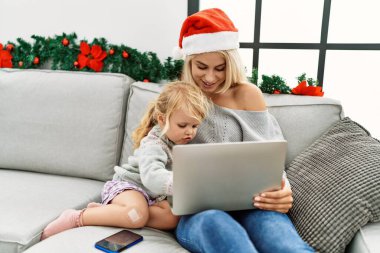 Mother and daughter using laptop sitting by christmas decor at home
