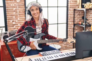 Middle age grey-haired woman musician playing electrical guitar at music studio