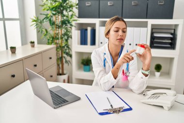 Young hispanic woman wearing doctor uniform writing on document holding test tube at clinic