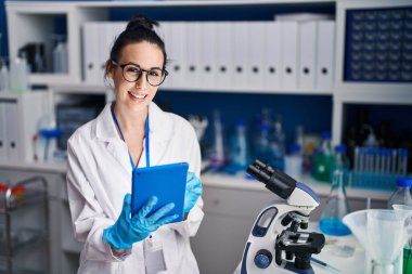 Genç beyaz kadın bilim adamı. Laboratuvarda dokunmatik ped kullanarak gülümsüyor.