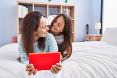 Woman and girl mother and daughter using touchpad at bedroom