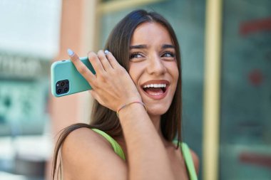 Genç, güzel, İspanyol bir kadın gülümsüyor. Caddedeki akıllı telefondan kendine güvenen bir sesli mesaj dinliyor.