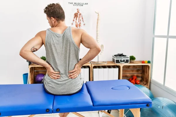 Young Hispanic Man Touching Injury Back Sitting Massage Board Clinic — стоковое фото