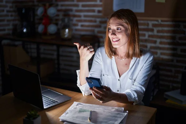 Young Redhead Woman Working Office Night Pointing Thumb Side Smiling — Foto de Stock