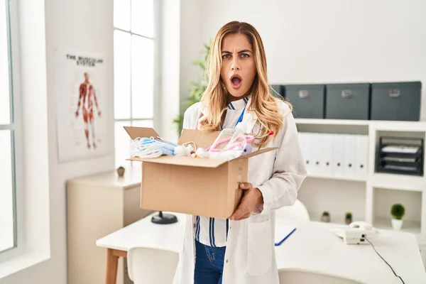 Young Blonde Doctor Woman Holding Box Medical Safety Items Shock — Stock Photo, Image
