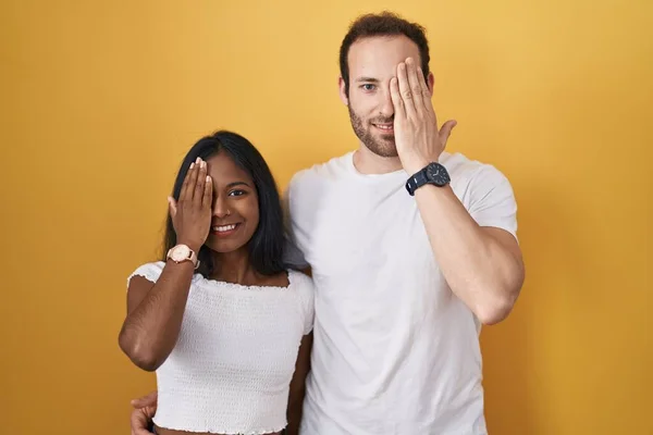 Interracial Couple Standing Yellow Background Covering One Eye Hand Confident — Zdjęcie stockowe