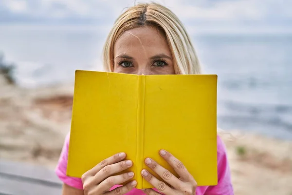 若いですブロンド女性カバー口とともに本で海辺 — ストック写真