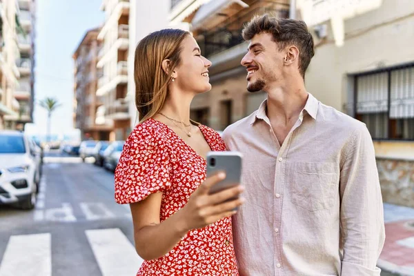 若いヒスパニック系のカップルが笑顔と市内でスマートフォンを使用して — ストック写真