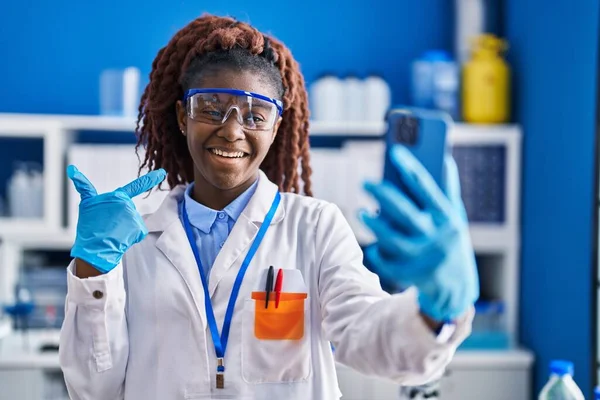 African woman working at scientist laboratory doing video call smiling happy pointing with hand and finger
