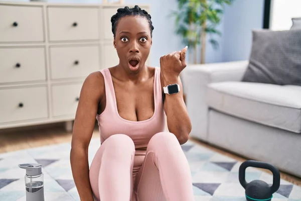Beautiful black woman using smart watch training at home scared and amazed with open mouth for surprise, disbelief face