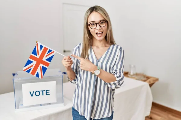 Asian young woman at political campaign election holding uk flag smiling happy pointing with hand and finger