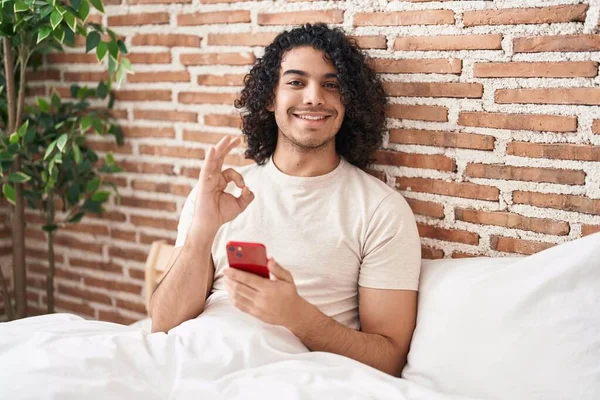 Kıvırcık Saçlı Akıllı Telefon Kullanan Spanyol Bir Adam Yatakta Oturmuş — Stok fotoğraf