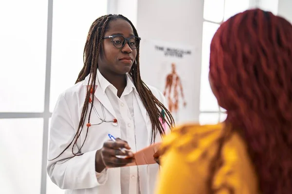 アフリカ系アメリカ人の女性医師と患者が診療所で診察報告書を書いている — ストック写真