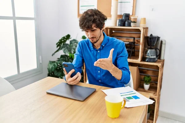 Young hispanic man unhappy using smartphone working at office
