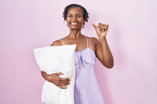 African Woman Dreadlocks Wearing Pajama Hugging Pillow Pointing Back Hand — Stockfoto
