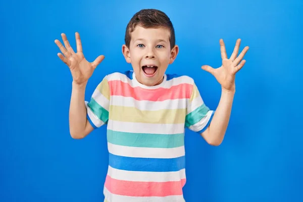 青い背景の上に立っている若い白人の子供はクレイジーを祝い 腕を上げて興奮して叫んで目を開けて成功したことに驚いています 勝者のコンセプト — ストック写真