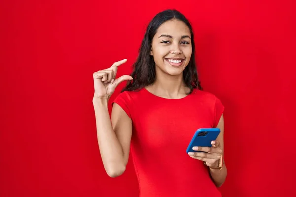 Jovem Brasileira Usando Smartphone Sobre Fundo Vermelho Sorrindo Gestos Confiantes — Fotografia de Stock