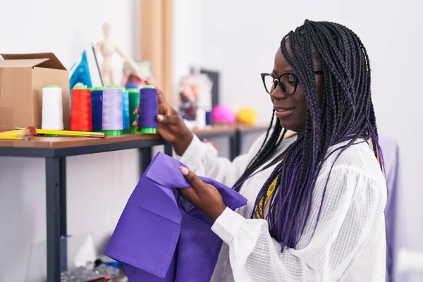 African american woman tailor smiling confident holding cloth and thread at tailor shop