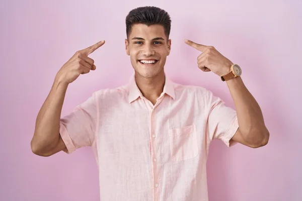Jonge Spaanse Man Staat Roze Achtergrond Glimlachend Wijzend Naar Het — Stockfoto