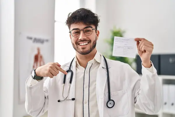 Лікар Латиноамериканець Бородою Тримає Ковальну Картку Показуючи Пальцем Усмішку Щасливій — стокове фото