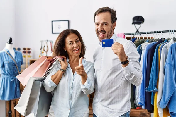 ヒスパニック系の中年のカップルが幸せな面白い顔でカメラに指を指してショッピングバッグやクレジットカードを保持 良いエネルギーと振動は — ストック写真