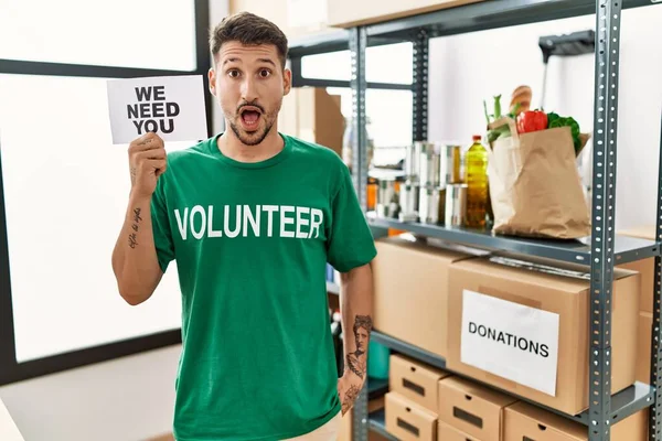 Joven Hombre Hispano Con Camiseta Voluntaria Sosteniendo Necesitamos Estandarte Asustado — Foto de Stock