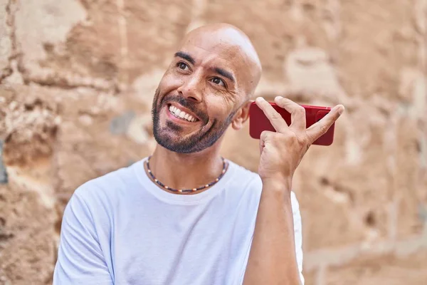 Young bald man smiling confident listening audio message by the smartphone over isolated stone background