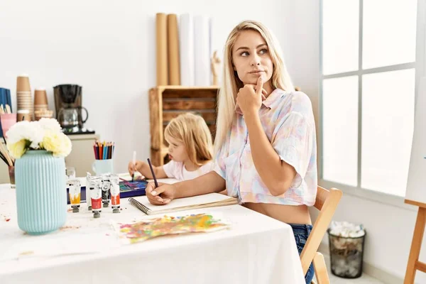 Caucasian family of mother and daughter painting at art studio serious face thinking about question with hand on chin, thoughtful about confusing idea