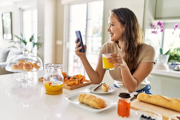 若いです美しいですヒスパニック女性持っています朝食スマートフォンを使用してキッチン — ストック写真