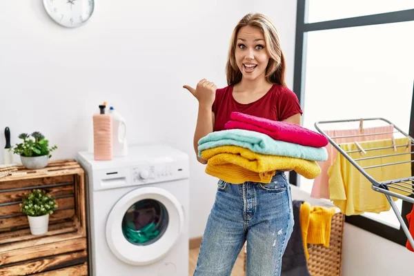 Young Caucasian Woman Holding Clean Laundry Pointing Thumb Side Smiling — Stock Photo, Image