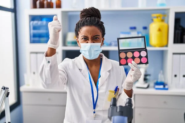 Young african american with braids working at scientist laboratory doing make up annoyed and frustrated shouting with anger, yelling crazy with anger and hand raised
