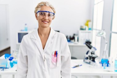 Orta yaşlı sarışın kadın bilim adamı laboratuvarında çalışıyor. Yüzünde mutlu ve havalı bir gülümseme var. şanslı kişi. 