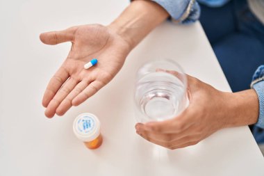 Young non binary man holding pill sitting on table at home