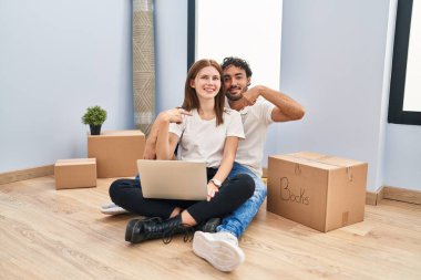 Yeni evinde dizüstü bilgisayar kullanan genç bir çift. Kendine güvenen, yüzünde gülümseme olan, kendini gururlu ve mutlu gösteren bir çift.. 