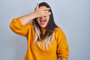 Soyutlanmış arka planda duran genç İspanyol kadın. Gülümsüyor ve gülümsüyor. Gözlerini şaşkınlıkla kapatıyor. kör kavram. 