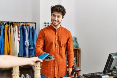 Customer hand paying to shopkeeper man using smartphone at clothing store.