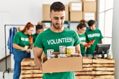 Group of young volunteers working at charity center. Man smiling happy and holding box with food to donate.